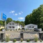 Hotel meerblau im Ostseebad Sellin auf Rügen: weiße Häuser in Bäderarchitektur mit verzierten Holzbalkonen, Hotelschild und Parkplatz vor Buchenwald